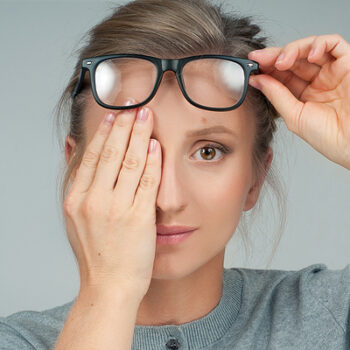 Woman with hand over eye next to an eye chart.